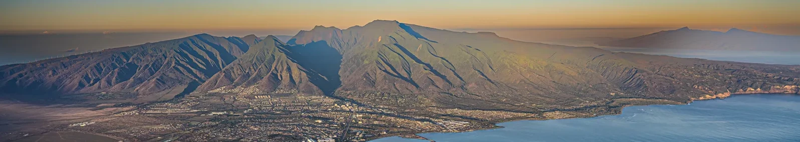 Aerial view of the West Maui Mountains and the towns below at golden hour, with Molokaʻi on the horizon